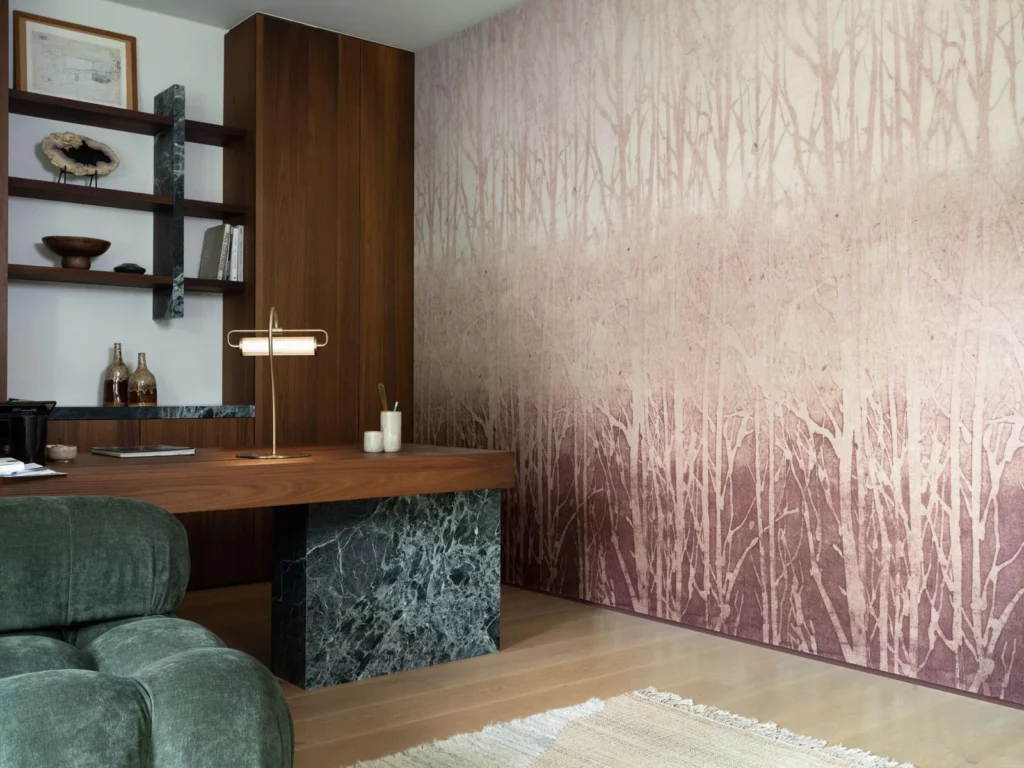 Arte Arbor: zarte Baumsilhouetten in Rosa- und Beigetönen neben einem grünen Sessel und einem hölzernen Arbeitsplatz.
