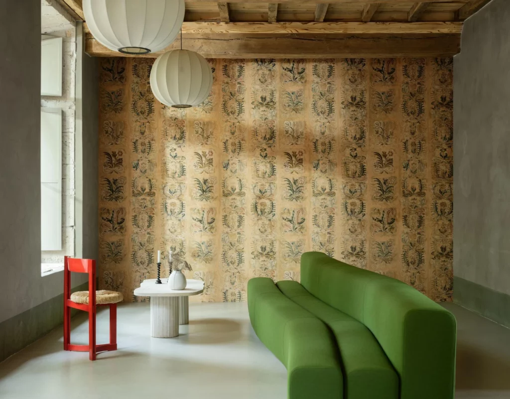 Arte Ornement: beiges Wanddekor mit vertikalen floralen Ornamenten hinter einem grünen Sofa.