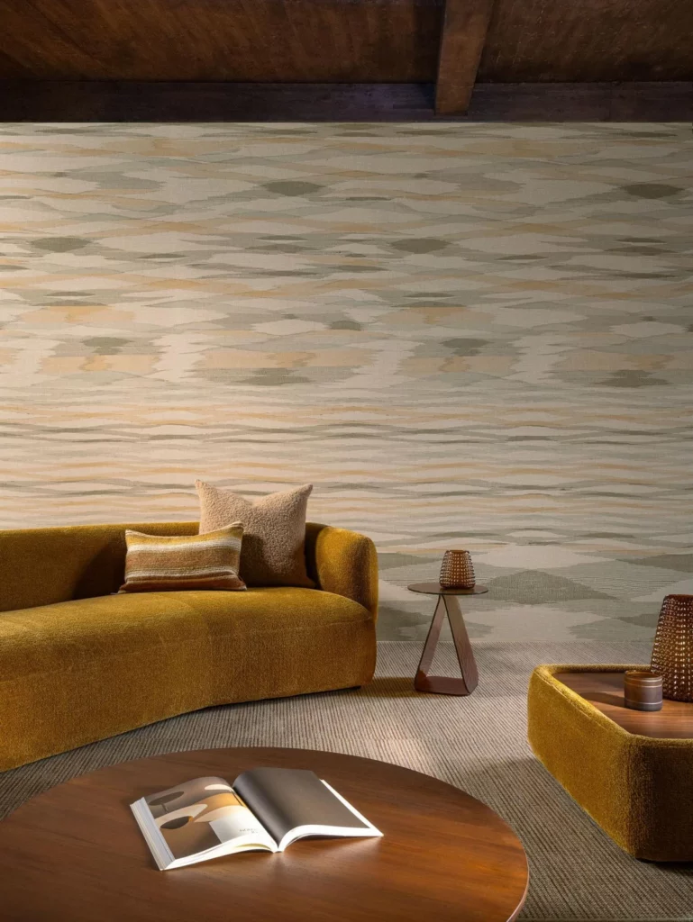 Arte Kashmir: weiche horizontale Farbbänder in Beige und Grün hinter einem geschwungenen senfgelben Sofa.