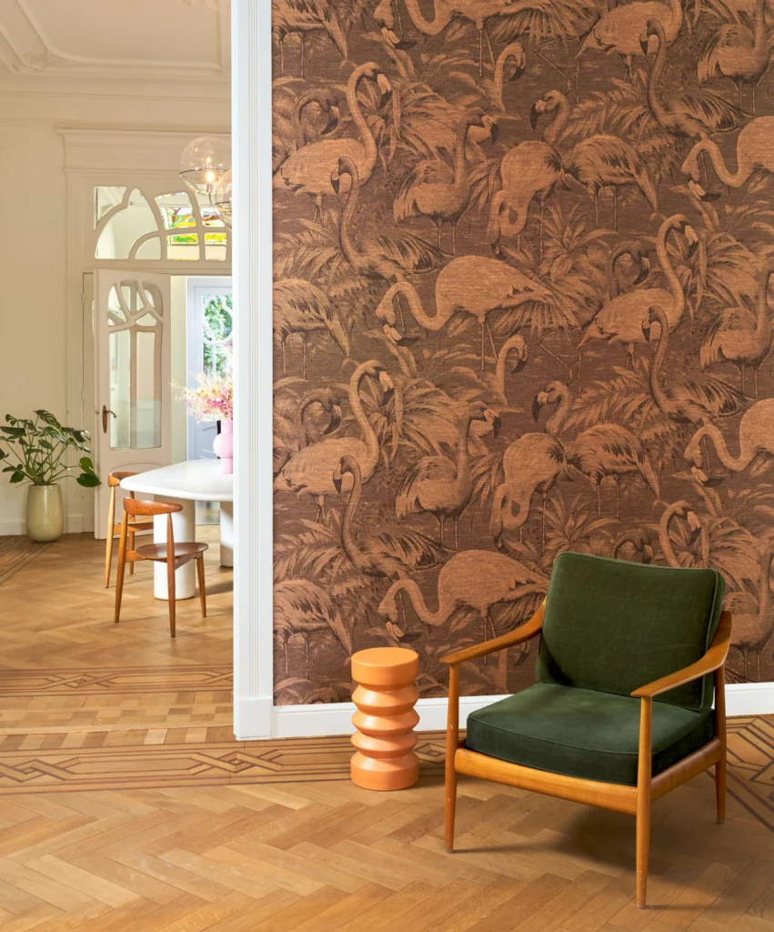 Arte Flamencos Andinos: flamingos und Pflanzen in warmen Terrakottatönen hinter einem dunkelgrünen Sessel.