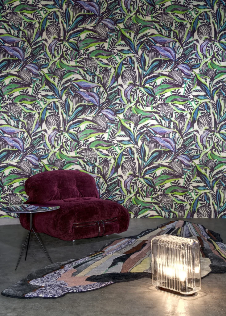 Arte Flor Imaginaria: violett-grünes tropisches Pflanzenmotiv hinter einem geschwungenen violetten Sessel.