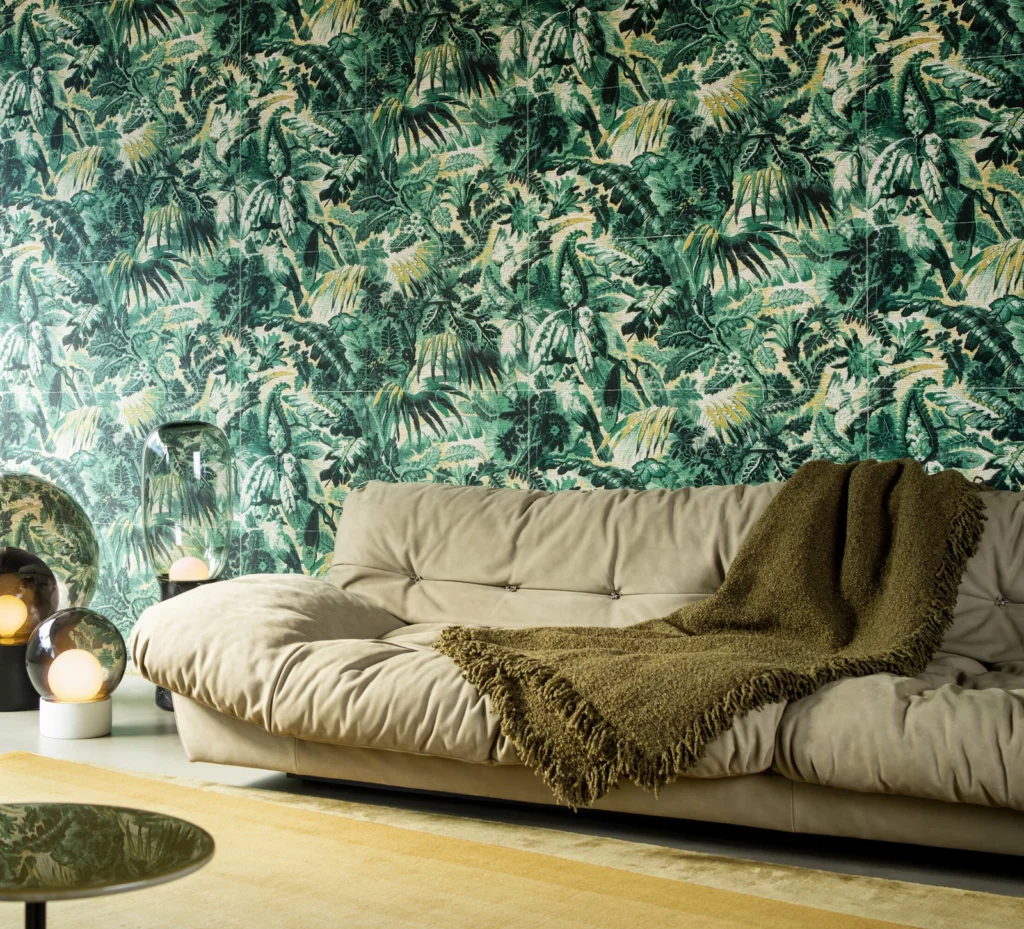 Arte Tropicali: dichtes tropisches Pflanzenmotiv in Grüntönen hinter einem beigefarbenen Sofa.
