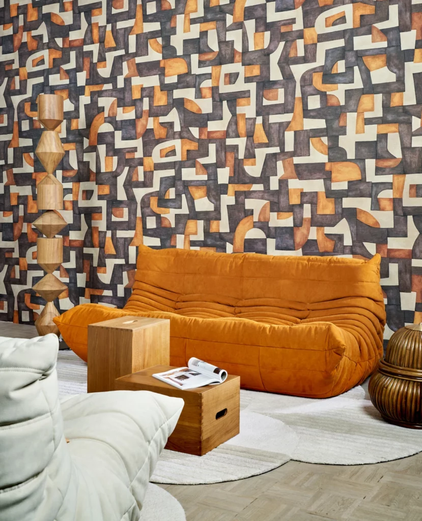 Arte Ecoline: geometrische Formen in Grau, Ocker und Weiß hinter einem orangefarbenen Sofa.