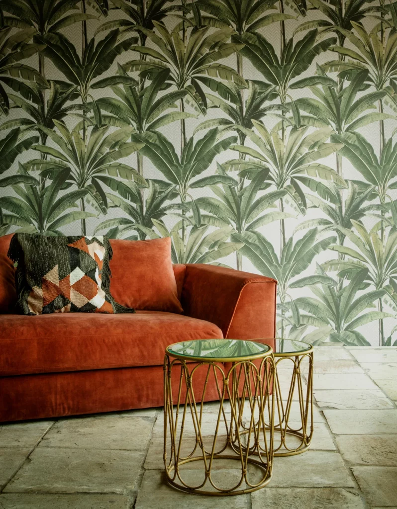 Arte Palmera: dunkelgrüne Palmenformen auf hellem Grund hinter einem rostfarbenen Sofa.