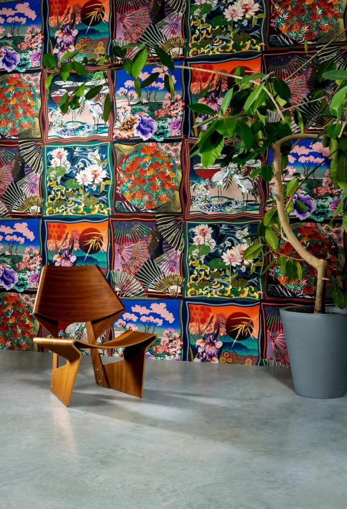 Arte Kimono: bunte, kachelartig angeordnete Bildfelder mit fernöstlichen Szenen hinter einem Holzsessel.