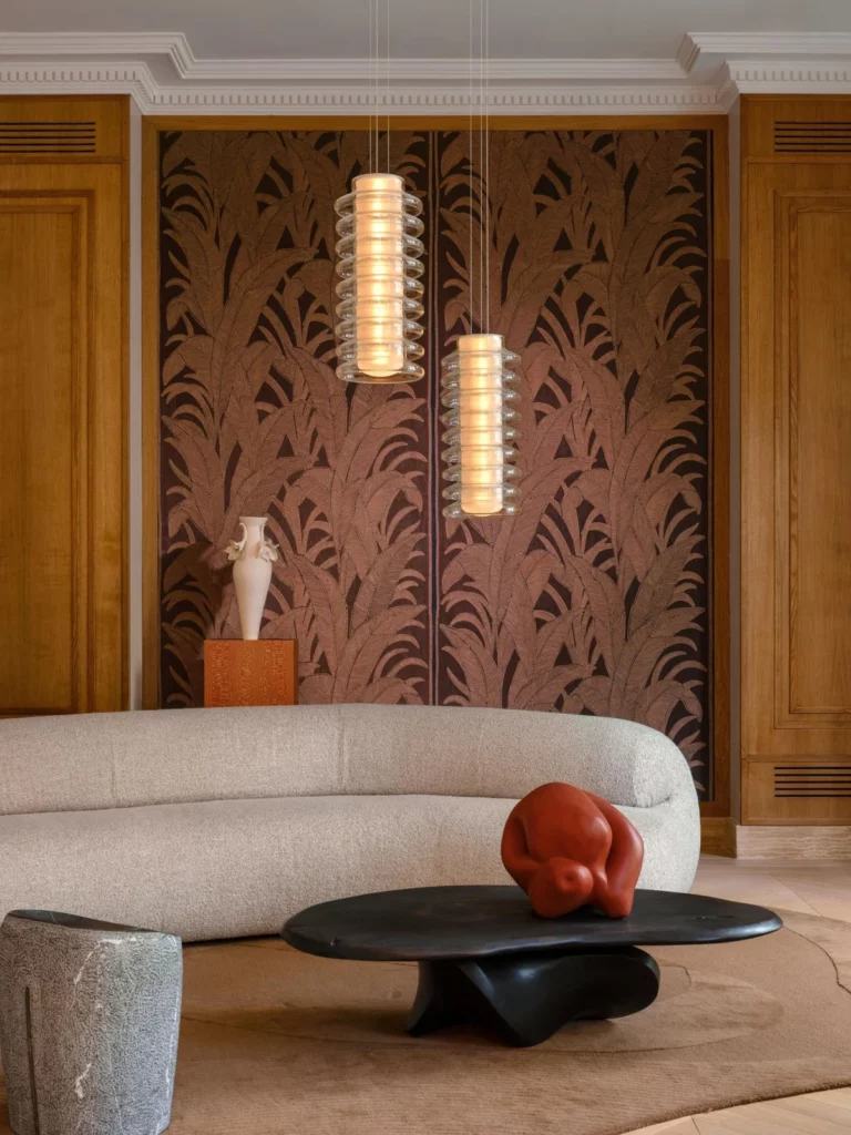 Arte Aranya: dunkle Palmblattmotive auf rosabraunem Grund hinter einem hellen Sofa.