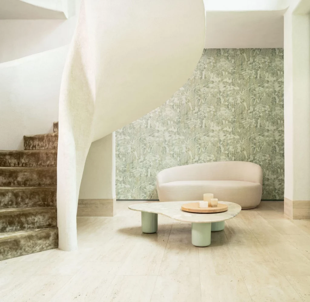 Arte Charmille: zartes grünes Blattmotiv an einer Treppenwand hinter einem hellen Sofa.