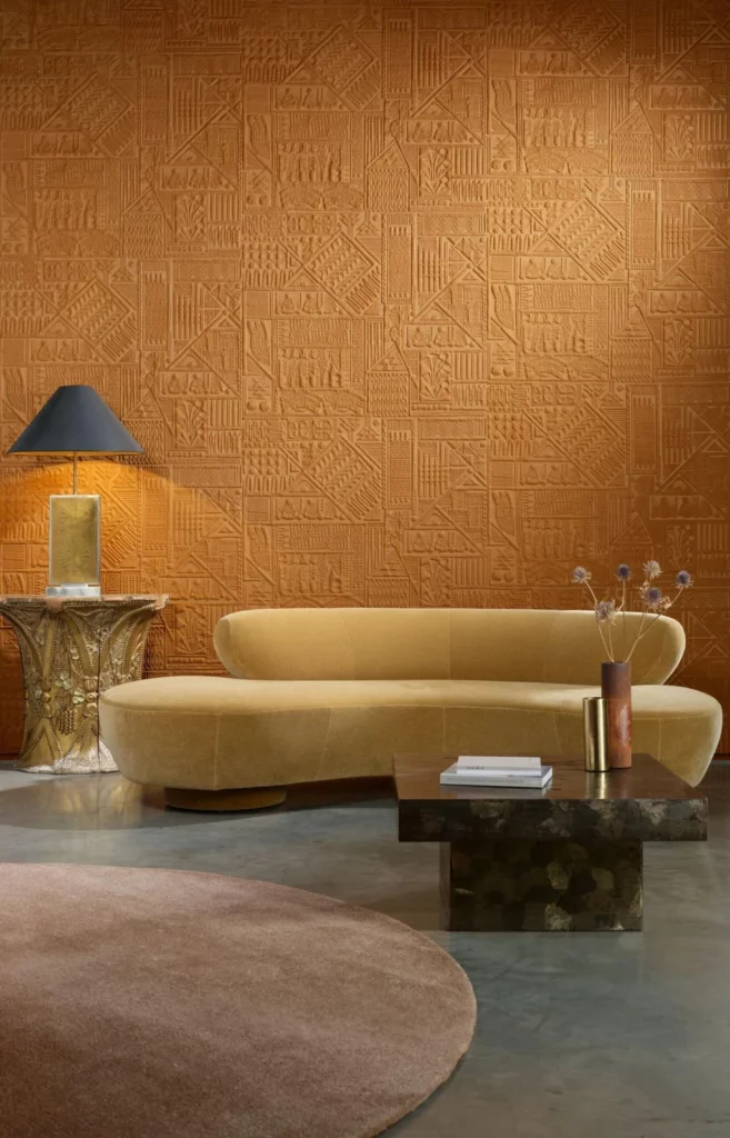 Arte Amarna: orangebraunes Wandrelief hinter einem geschwungenen gelben Sofa.