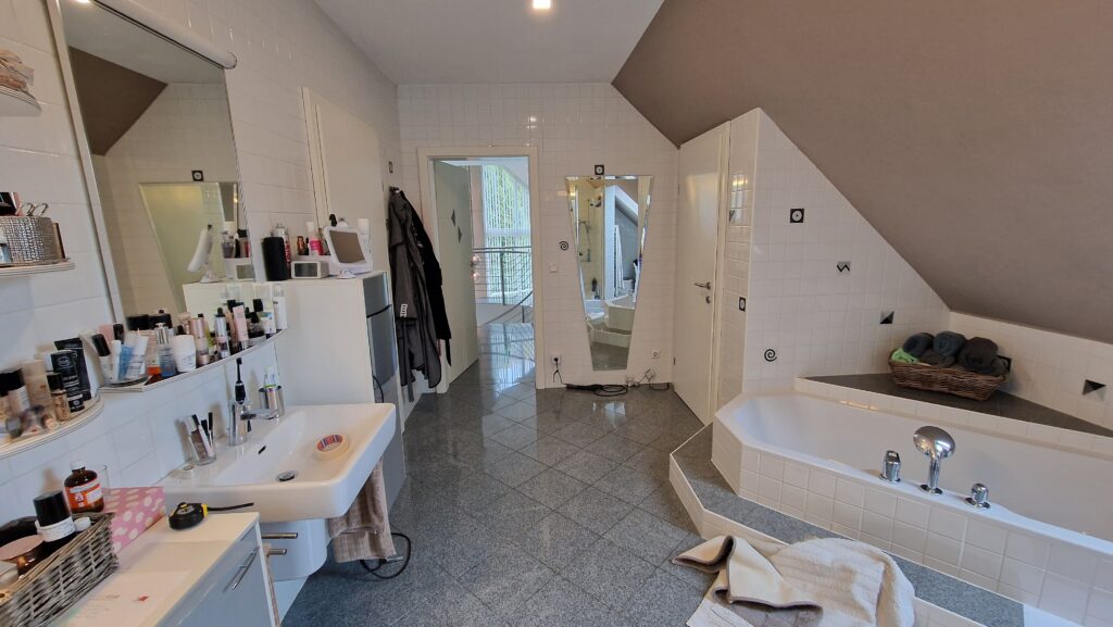 Ursprüngliches Bad mit Waschbecken, Einbauwanne und mehreren Türen, Blick zum Eingang.