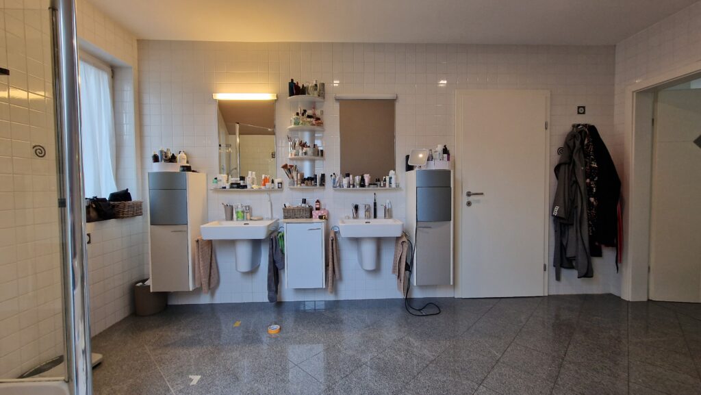 Zwei einzelne Waschbecken mit Spiegeln und offenen Ablagen vor einer gefliesten Wand.