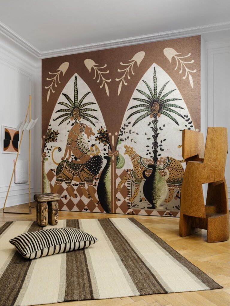 Arte Armalu: gerahmtes Wandbild mit stilisierten Figuren und Pflanzen in Naturtönen hinter einem hellen Sofa.