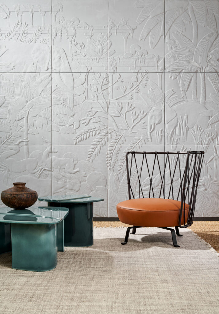 Arte Between Rivers: helles Wandrelief hinter einem orange gepolsterten Metallstuhl und türkisfarbenen Beistelltischen.