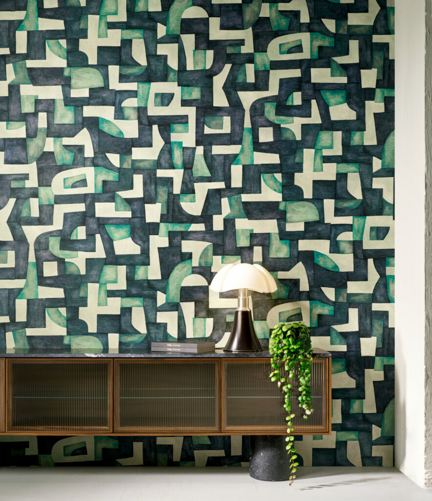Arte Ecoline: geometrisches Wandmotiv in Grün-, Blau- und Naturtönen hinter einem dunklen Sideboard.