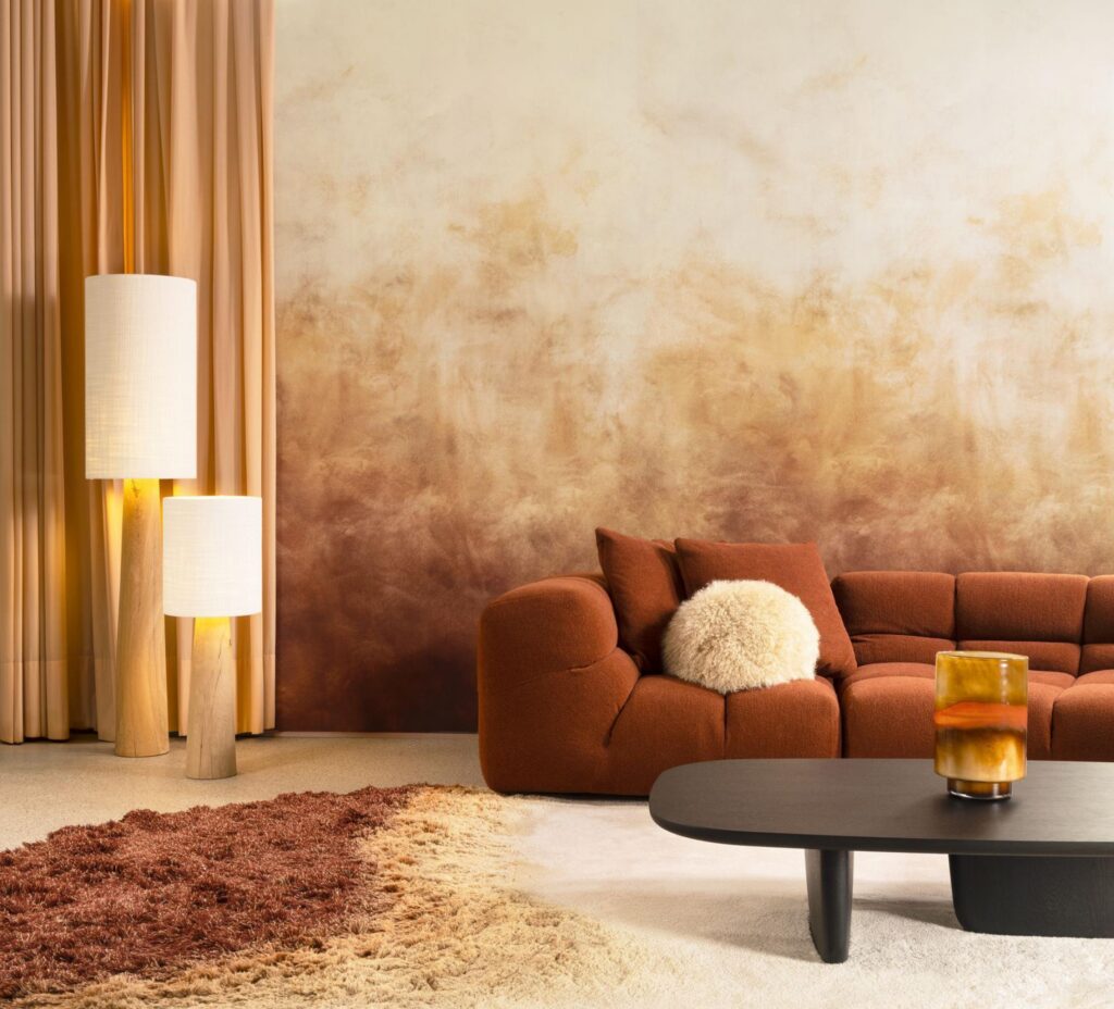 Arte Flux: sanfter Farbverlauf in Ocker- und Cremetönen hinter einem orangebraunen Sofa.