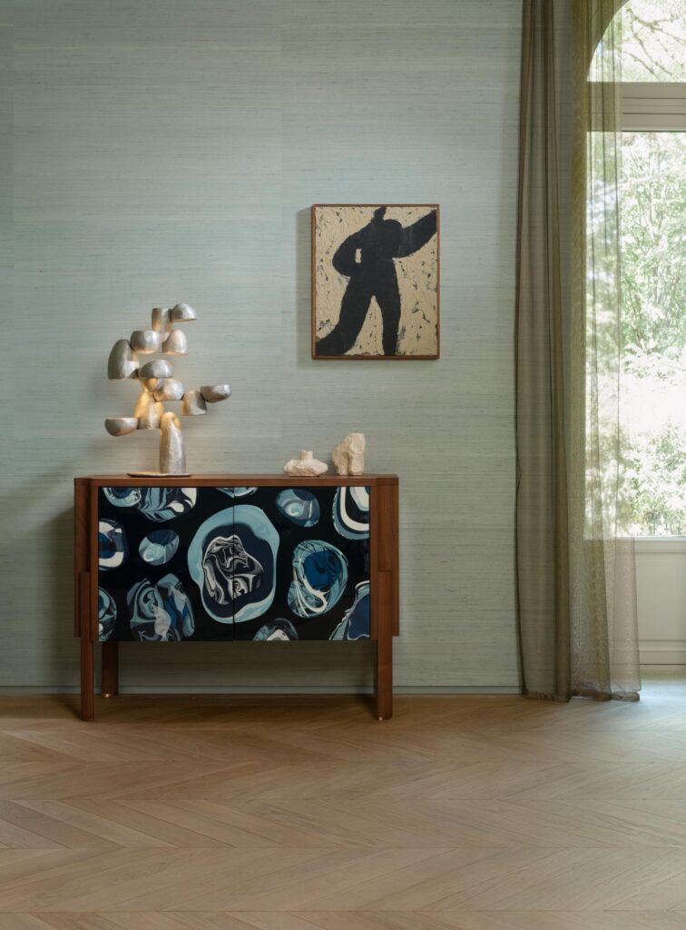 Arte Mandya: hellblaue Strukturwand hinter einer Holzkommode mit floral gestalteten Türen.
