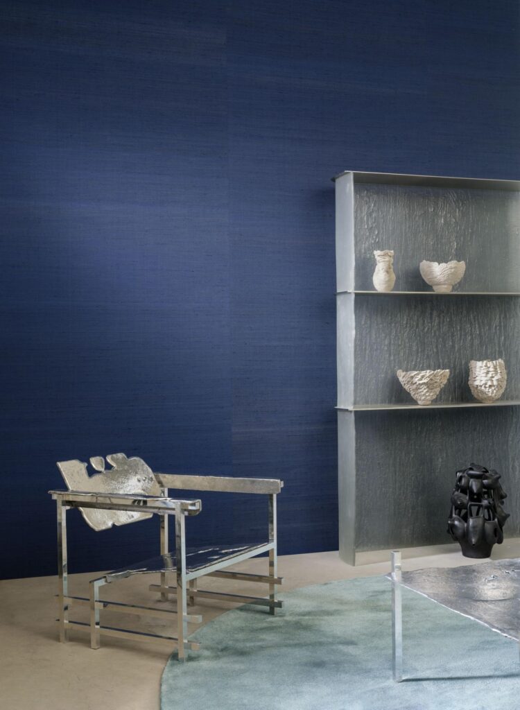 Arte Mandya: dunkelblaue Strukturwand hinter einem Metallstuhl und einem offenen Regal.