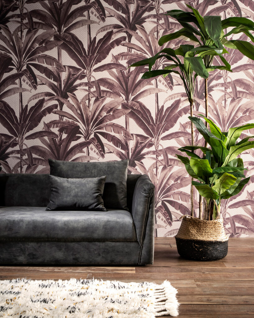 Arte Palmera: rosa- und violettfarbene Palmblätter hinter einem dunklen Sofa und einer großen Zimmerpflanze.