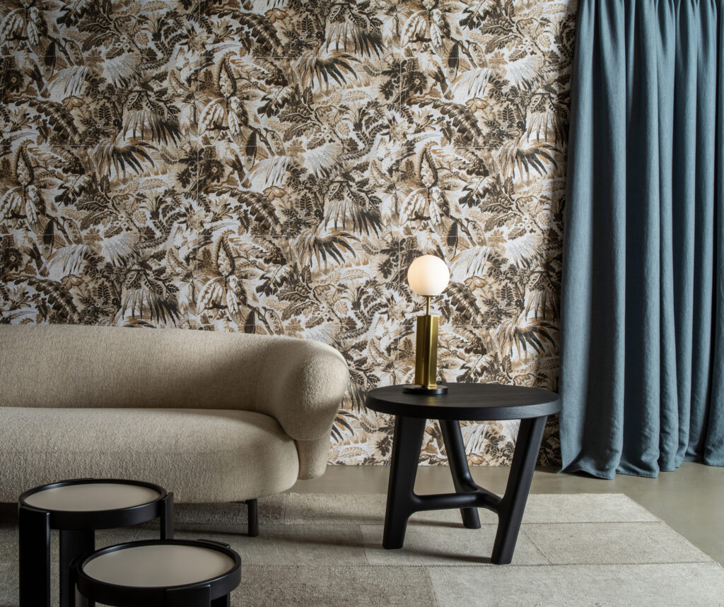 Arte Tropicali: dunkles tropisches Blattmotiv hinter einem hellen Sofa neben blauen Vorhängen.