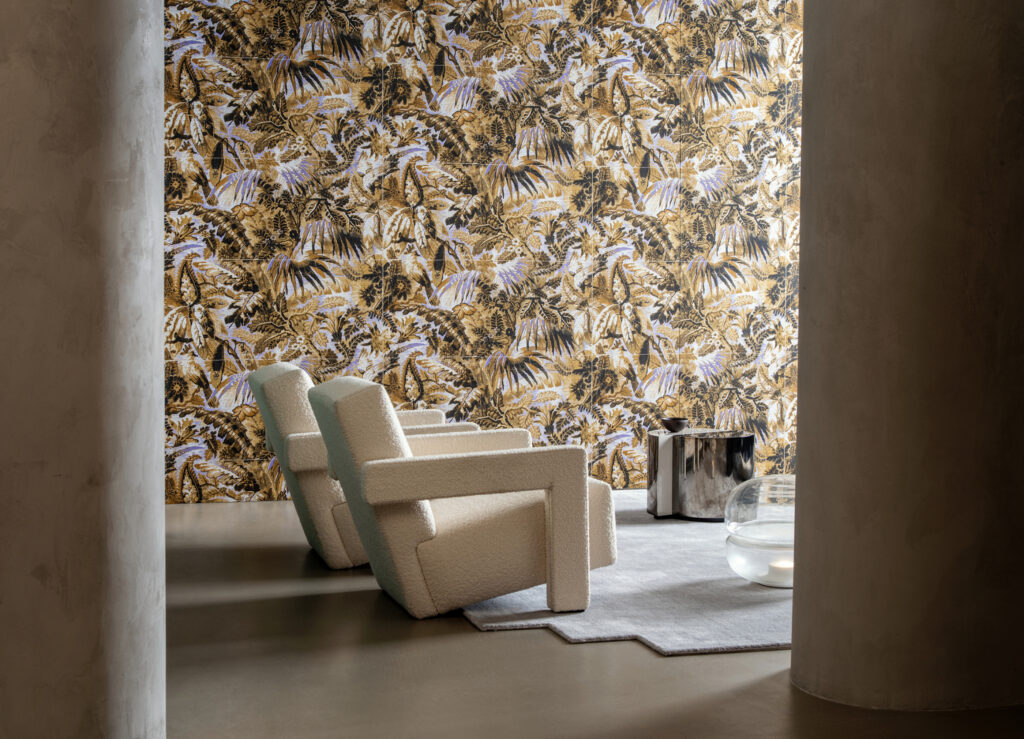 Arte Tropicali: tropisches Blattmotiv in Gelb- und Naturtönen hinter einem hellen Sessel.