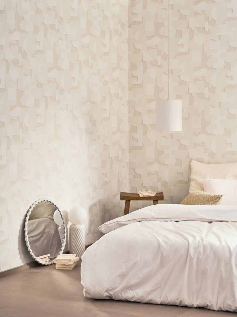 Schlafzimmer mit heller geometrischer Tapete und weißem Bett aus der Kollektion Basalte.