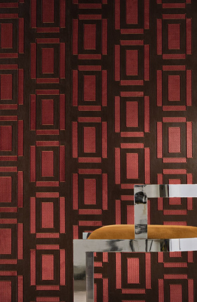 Rot-schwarzes geometrisches Wandmuster hinter einem glänzenden Gestell mit Sitzpolster.
