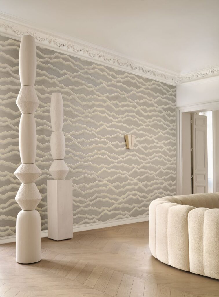 Heller Wohnraum mit grauem Wellenmuster an der Wand, weißem Sofa und hohen skulpturalen Dekorobjekten aus der Kollektion Midori.
