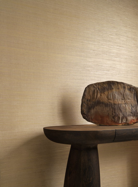 Helle seidige Wandstruktur hinter einem dunklen Holztisch mit organisch geformter Skulptur.