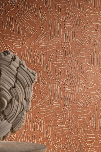 Terrakottafarbene Wand mit gestickter abstrakter Linienzeichnung neben einer hellen Skulptur.