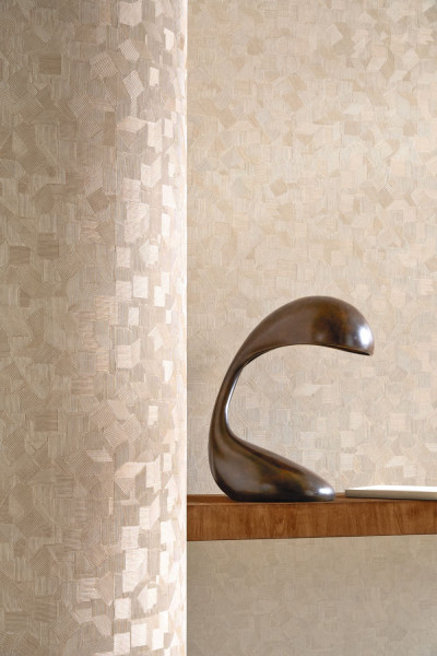 Helle Wand mit kleinteiligem geometrischem Muster hinter einer dunklen Skulptur.