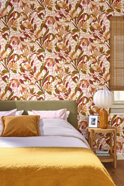 Mehrfarbige Blüten- und Blättertapete hinter einem Bett mit gelber Decke.