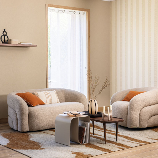 Helle Streifentapete im Wohnbereich mit zwei abgerundeten Sofas und orangefarbenen Kissen.