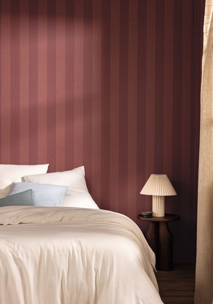 Bordeauxrote Streifentapete Rayure chevron hinter einem Bett mit weißer Bettwäsche.
