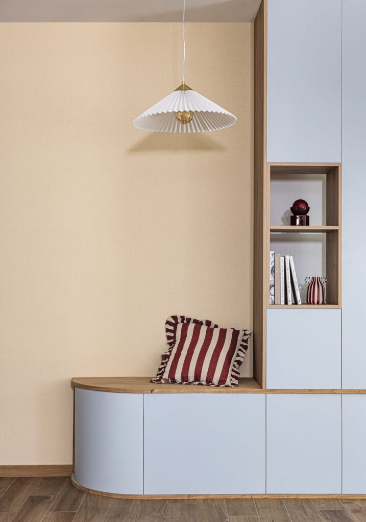 Cremefarbene Uni-Tapete aus Cocoon neben einer hellblauen Sitzbank und einem Bücherregal.
