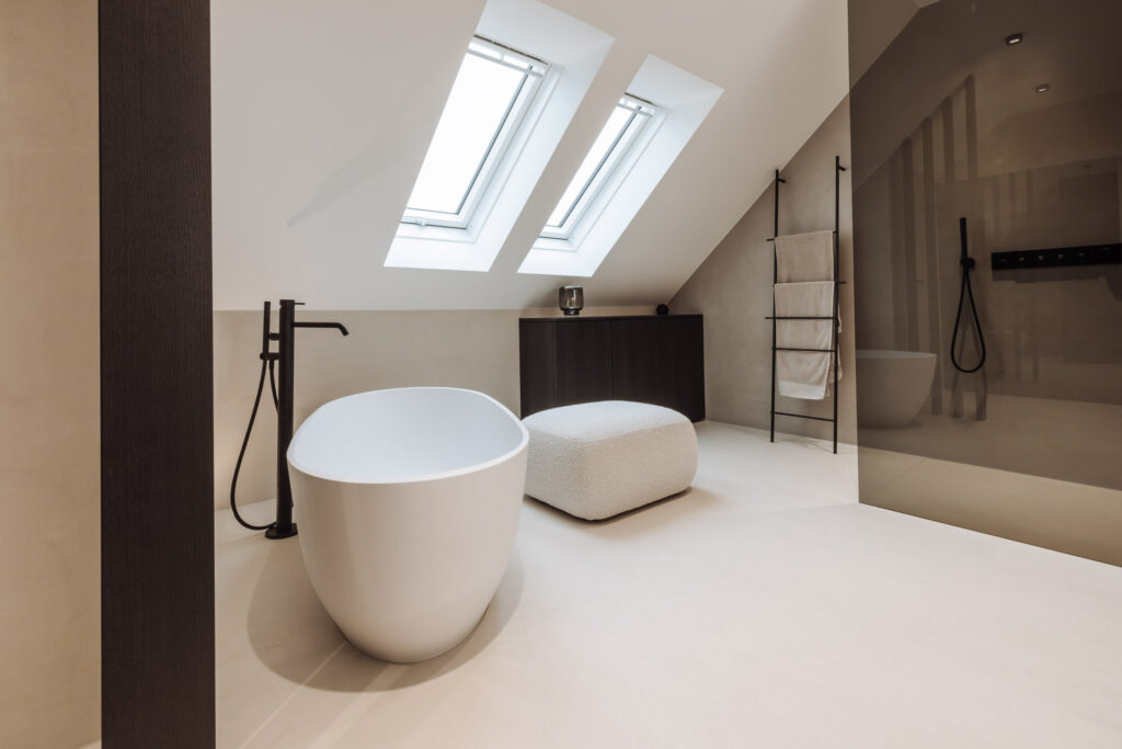 Dachgeschossbad mit zwei Dachfenstern, freistehender Wanne, hellem Hocker und verglaster Dusche.
