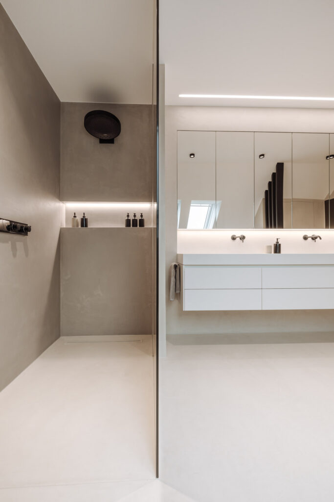 Glasabtrennung zwischen der Dusche mit beleuchteter Ablage und dem weißen Waschtisch.