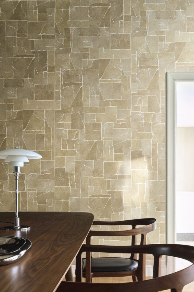 Geometrisch gegliederte goldbeige Wandfläche hinter einem dunklen Esstisch und Holzstühlen.