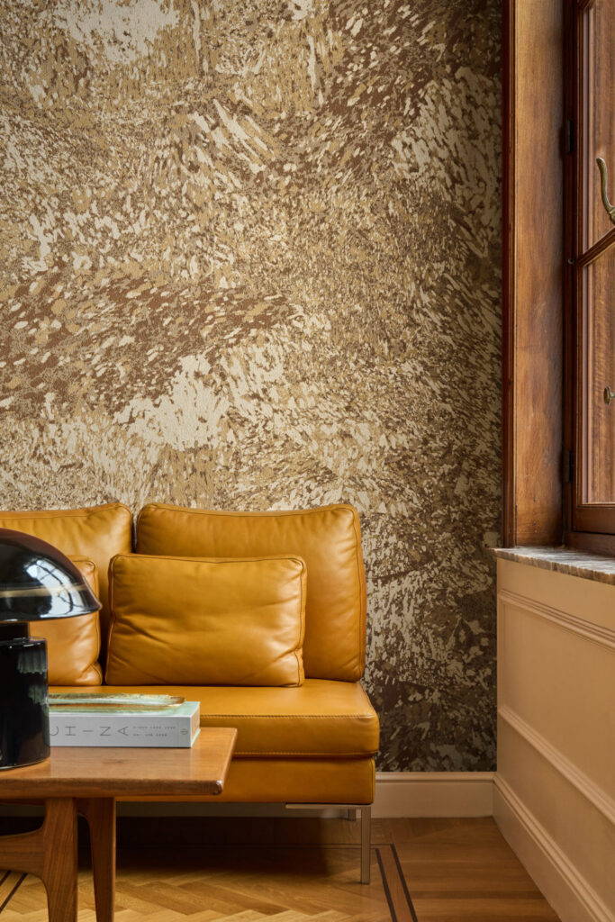 Lebhaft marmorierte Wand in Gold- und Brauntönen hinter einem senfgelben Ledersofa.