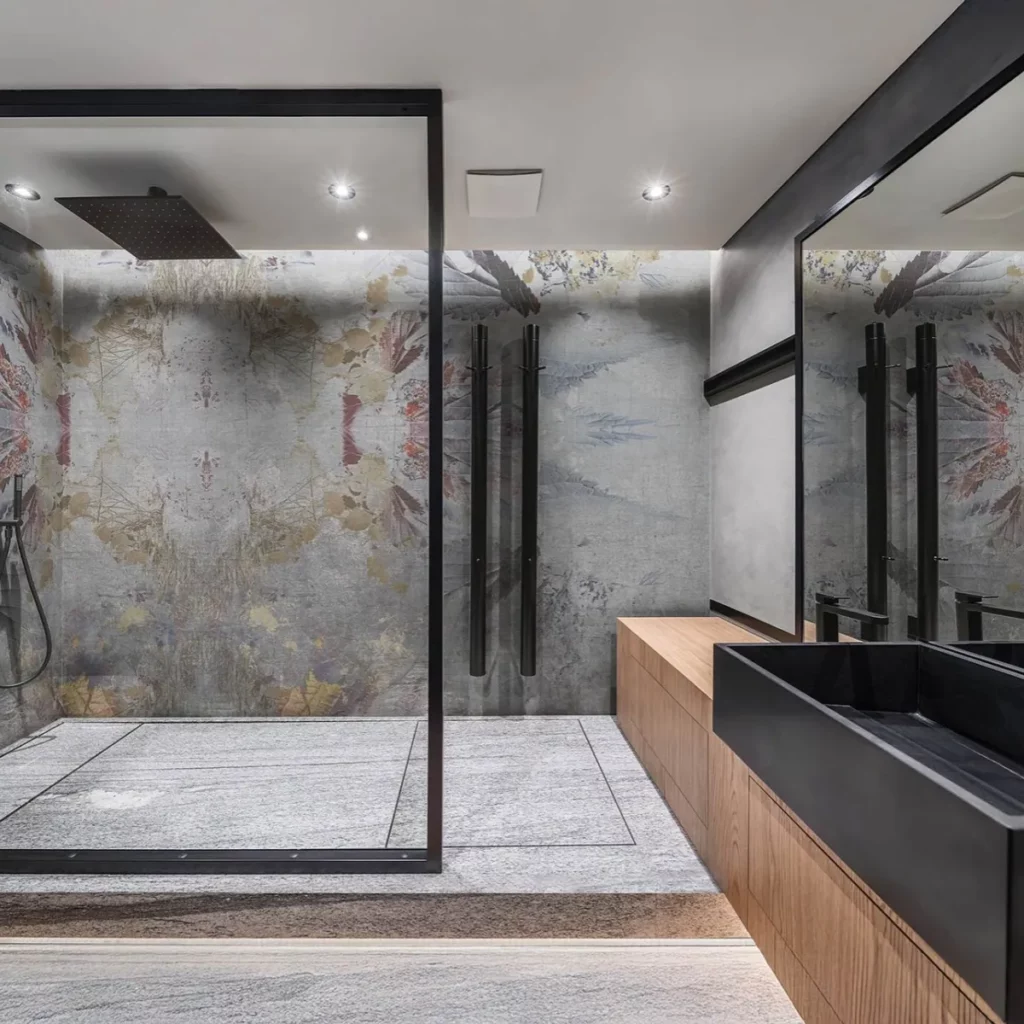 Skye von Tecnografica: blasse florale und ornamentale Spuren auf grauem Grund in einem Badezimmer mit Glasdusche.