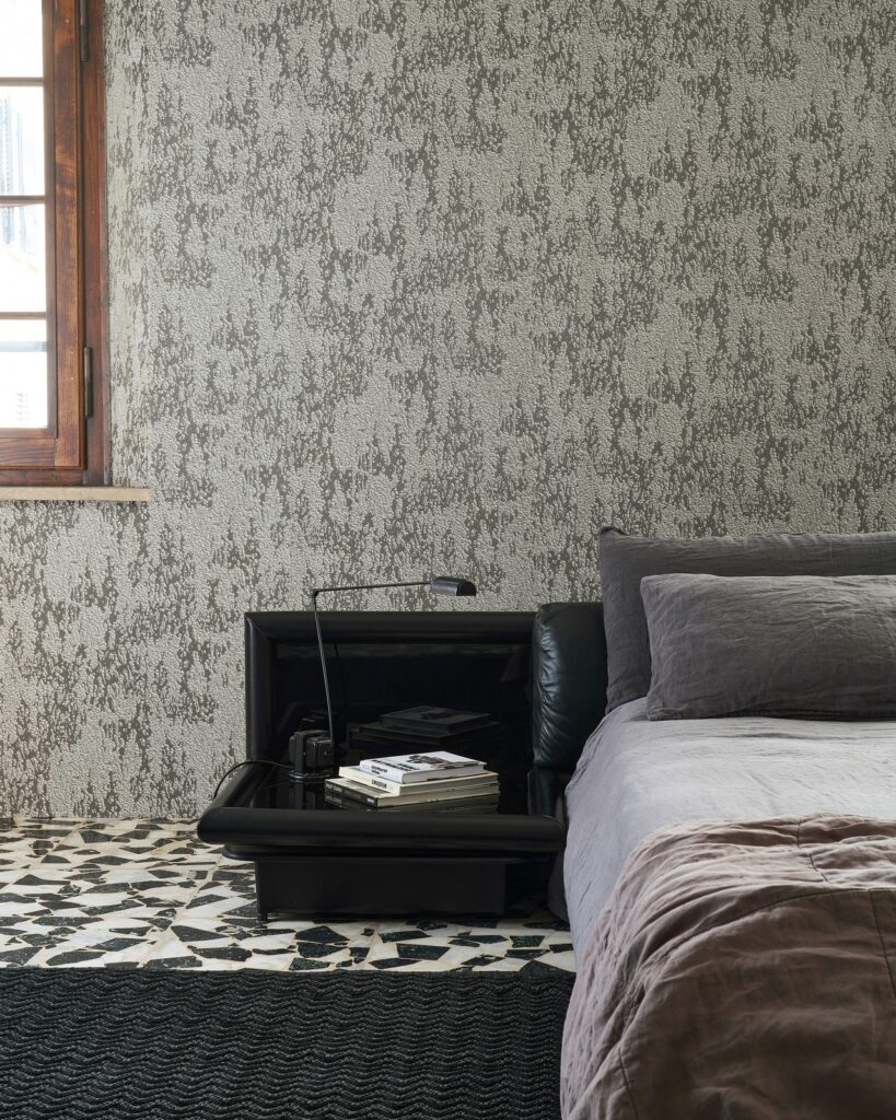 Graue strukturierte Wandbekleidung Mose am Kopfende eines Bettes – Wall&decò Essential Wallpaper 2025