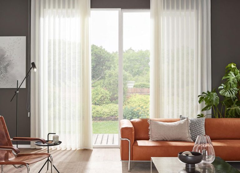 LEHA Softshade vor einer großen Fensterfront in einem Wohnraum mit rostfarbenem Sofa.