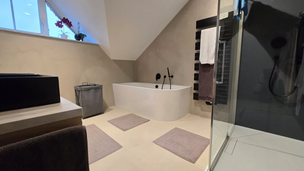 Bad mit weißer Badewanne unter der Dachschräge, dreieckigem Fenster und seitlicher Glasdusche.