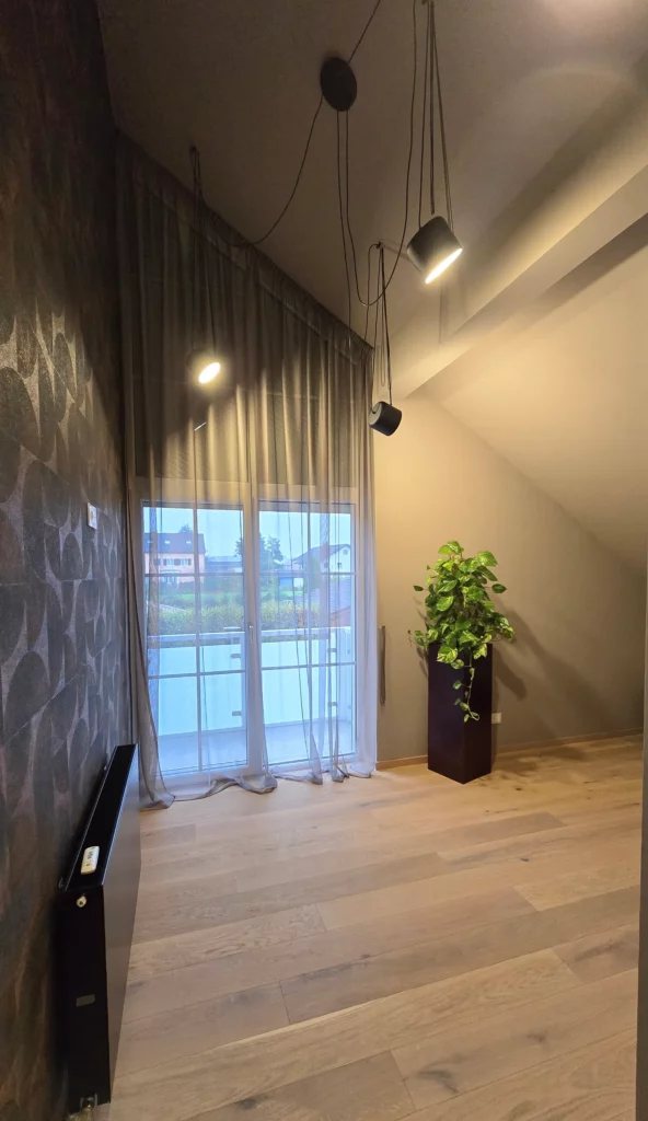 Gästezimmer mit dunklem geometrischem Wandmuster, schwarzen Pendelleuchten und hohem Fenster mit Vorhang.