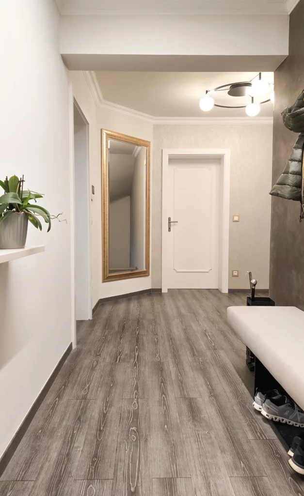 Blick durch die helle Garderobe auf einen großen goldgerahmten Spiegel, weiße Türen und eine gepolsterte Sitzbank.