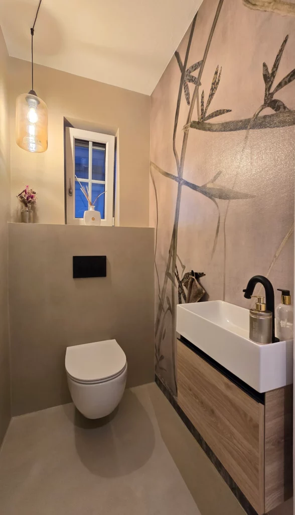 WC mit kleinem Fenster, gläserner Pendelleuchte und weißem Waschbecken vor einer Wand mit Bambusmotiv.