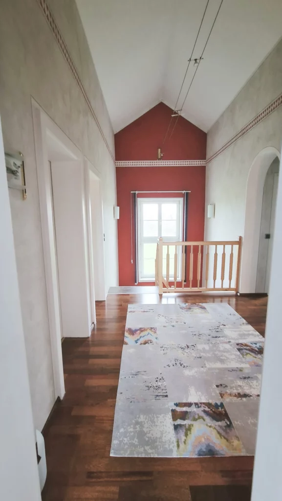 Obere Galerie vor der Neugestaltung mit roter Giebelwand, hohem Fenster am Treppenabgang und Holzgeländer.