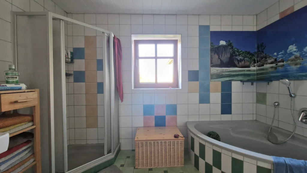 Badezimmer vor der Neugestaltung mit Duschkabine links, Fenster in der Mitte und Eckbadewanne rechts.